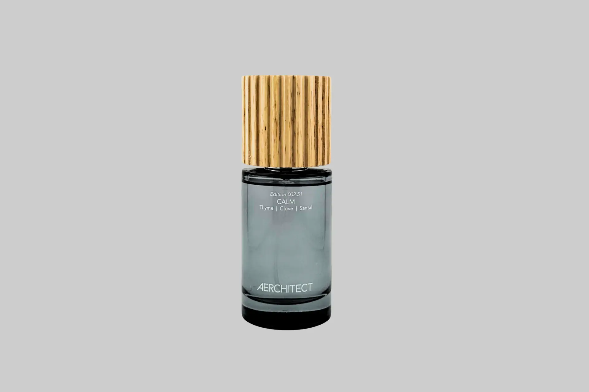 An Aerchitect CALM mist bottle with a wooden cap against a greige background, showing its minimal label and 100ml format with thyme and botanical notes arranged nearby.