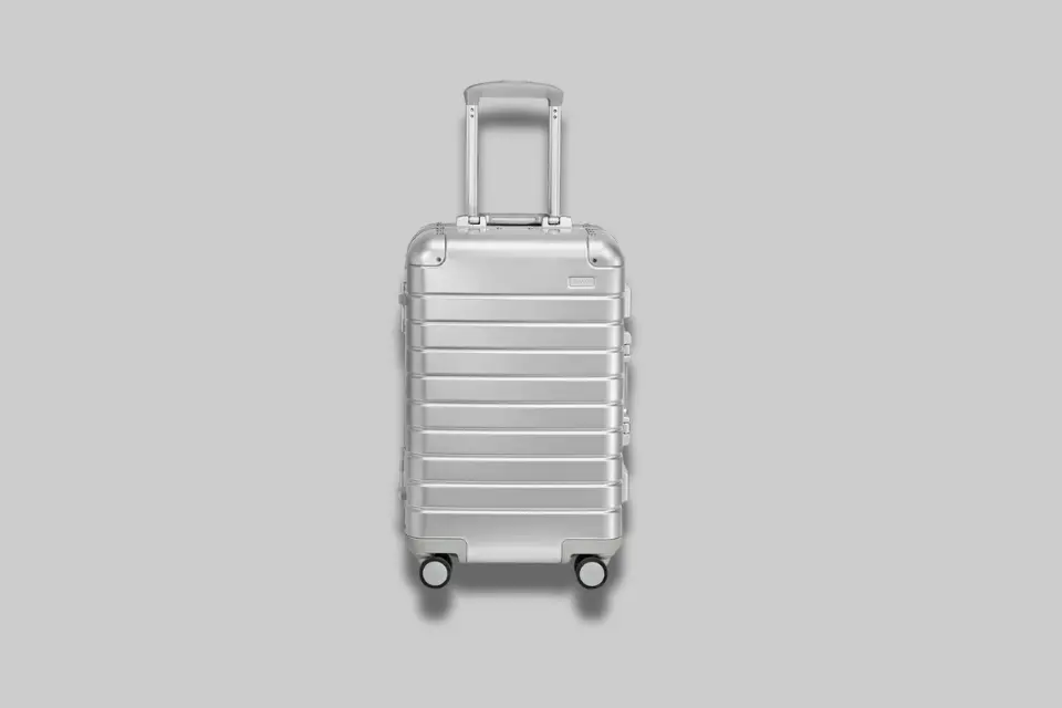 Silver Away Aluminum Bigger Carry-On suitcase gliding through an airport terminal, showcasing its sleek design and 360-degree spinner wheels. - Product Review