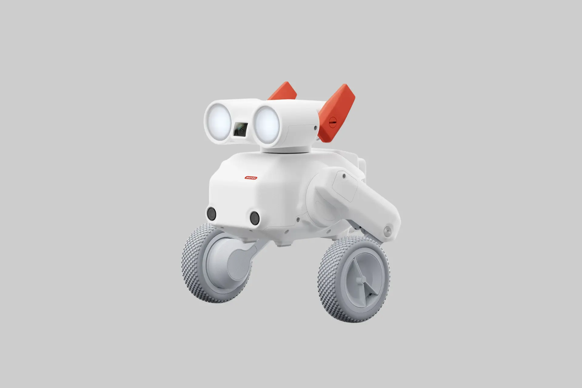 The Mondo Robotics Beni all-terrain camera robot on a grassy surface, showing its compact two-wheeled form factor, front camera, and wristband motion controller alongside it.