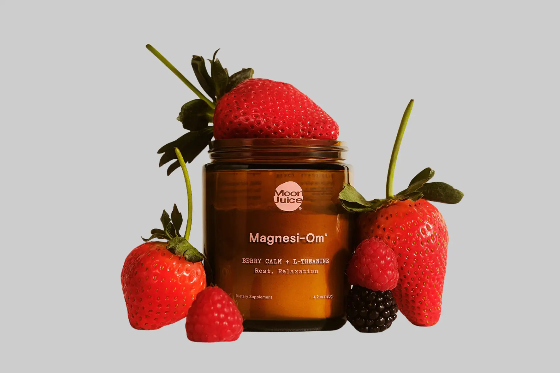 A glass of Moon Juice Magnesi-Om in a berry or blue lemon flavor, mixed with water, with the branded jar in the background. - Product Review