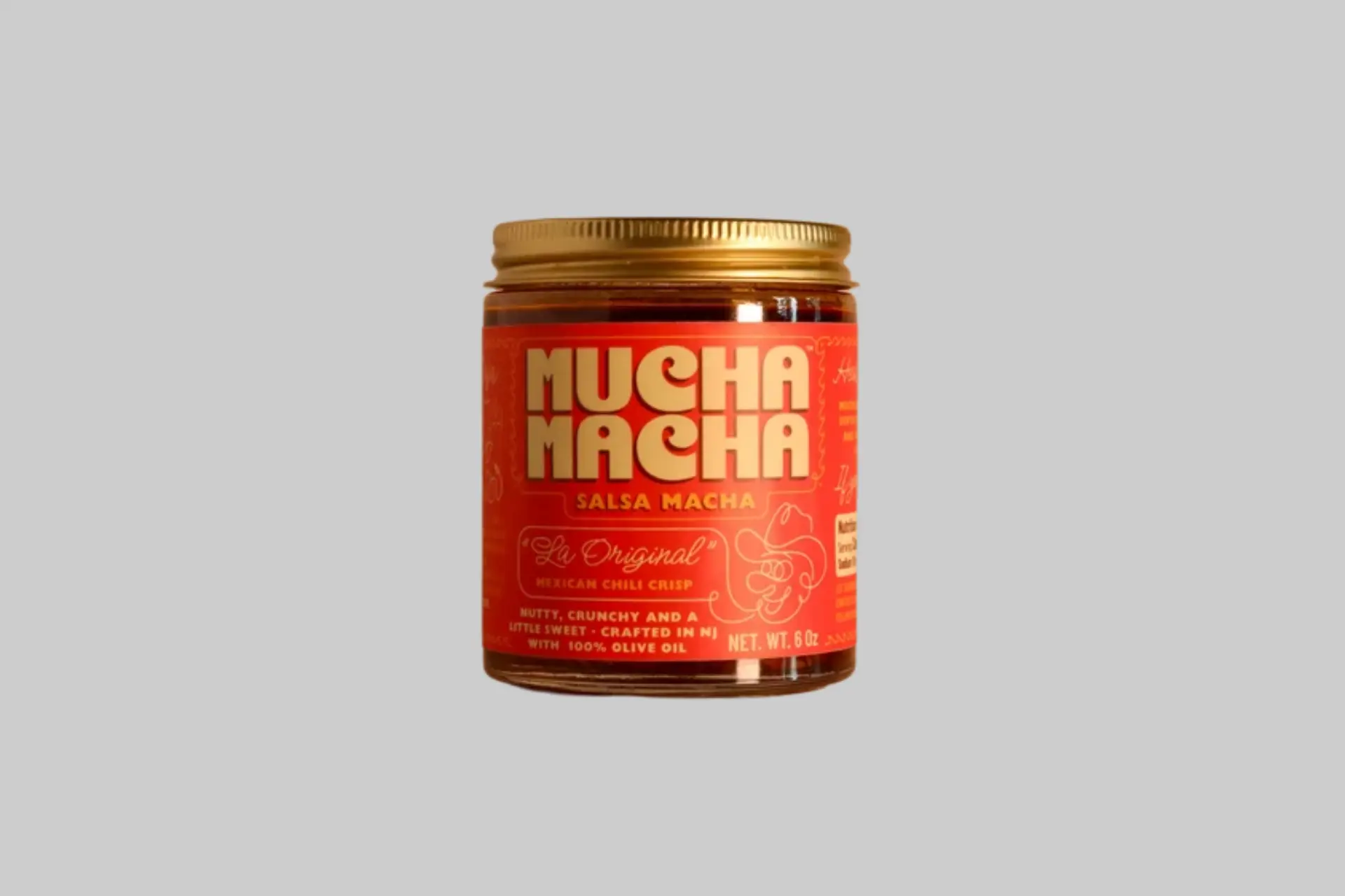 A 6oz jar of Mucha Macha Original Salsa Macha on a warm beige background, showing the deep red chili oil with visible crunchy bits through the glass.