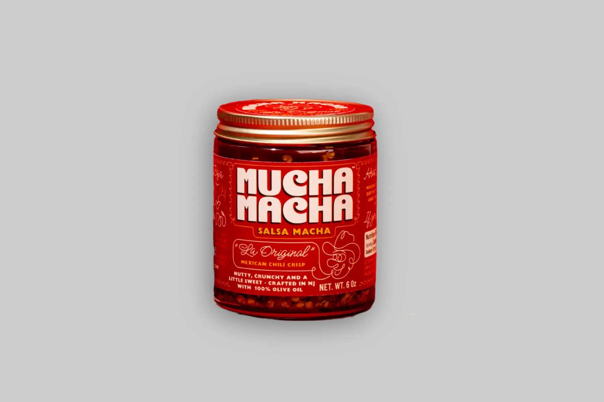 A 6oz jar of Mucha Macha Original Salsa Macha on a warm beige background, showing the deep red chili oil with visible crunchy bits through the glass.